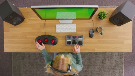 Overhead-View-Of-Female-Video-Editor-Working-At-Computer-With-Green-Screen-In-Creative-Office