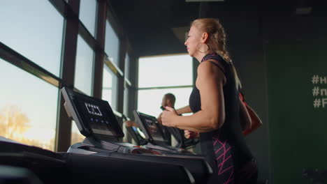 A-group-of-people-running-on-treadmills-near-a-large-panoramic-window.-Group-cardio-workout