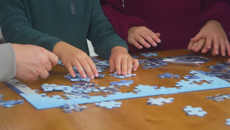 Close-Up-Of-Family-Sitting-Around-Table-At-Home-Doing-Jigsaw-Puzzle-Together