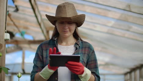 Beautiful-woman-florist-walks-through-the-greenhouse-with-a-tablet-computer-checks-the-grown-roses-keeps-track-of-the-harvest-and-check-flower-for-business-clients