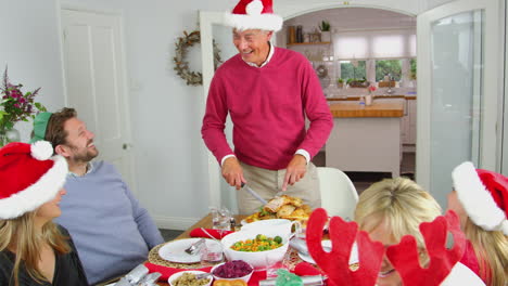 Grandfather-Carving-Turkey-As-Multi-Generation-Family-Sit-Down-To-Eat-Christmas-Meal-Together