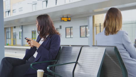 Zwei-Geschäftsfrauen-Pendeln-Zur-Arbeit-Und-Warten-Auf-Dem-Bahnsteig-Auf-Den-Zug-Und-Schauen-Auf-Mobiltelefone