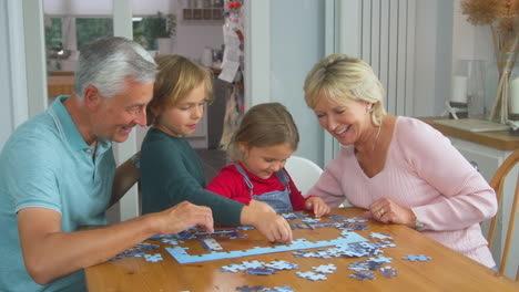 Enkelkinder-Mit-Großeltern-Sitzen-Zu-Hause-Am-Tisch-Und-Machen-Gemeinsam-Puzzles