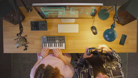 Overhead-View-Of-Male-And-Female-Musicians-At-Computer-With-Keyboard-In-Studio-At-Night
