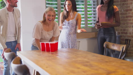 Multi-Cultural-Group-Of-Friends-Playing-Game-At-Home-Together-Throwing-Ball-Into-Paper-Cup