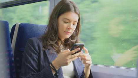 Businesswoman-With-Wireless-Earbuds-Commuting-To-Work-On-Train-Looking-At-Mobile-Phone