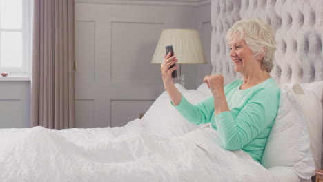 Ältere-Frau-Zu-Hause-Im-Schlafanzug-Im-Bett,-Die-Einen-Videoanruf-Mit-Dem-Mobiltelefon-Tätigt