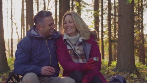 Loving-mature-couple-stop-for-rest-and-hot-drink-on-walk-through-fall-or-winter-countryside---shot-in-slow-motion