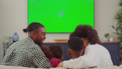 Rear-view-of-family-sitting-on-sofa-at-home-watching-green-screen-TV-and-laughing-at-comedy---shot-in-slow-motion