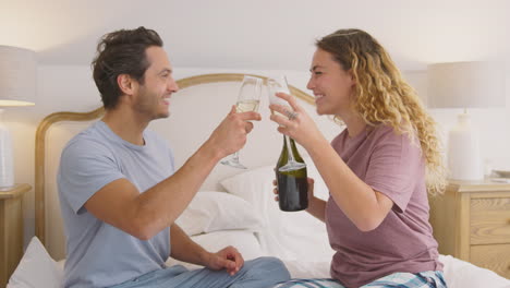 Loving-Couple-Wearing-Pyjamas-In-Bed-At-Home-Celebrating-Birthday-Or-Anniversary-With-Champagne