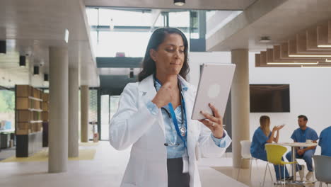 Portrait-Of-Female-Doctor-Wearing-White-Coat-With-Digital-Tablet-In-Busy-Hospital-Building