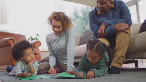 Grandparents-Sitting-On-Floor-At-Home-With-Grandchildren-As-They-Draw-Picture-Together