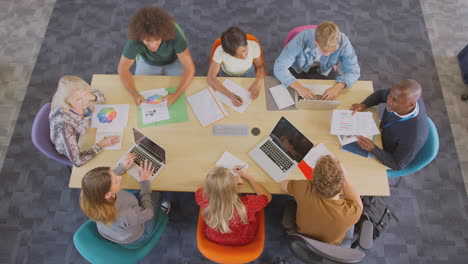Overhead-Shot-Of-University-Or-College-Students-Sitting-Around-Table-With-Tutors-In-Lesson