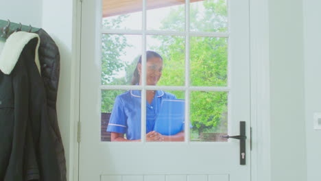 Senior-Woman-At-Home-Using-Walking-Stick-Greeting-Female-Nurse-Or-Care-Worker-In-Uniform-At-Door