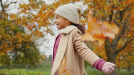 Young-girl-having-fun-throwing-autumn-leaves-into-the-air-on-walk-in-countryside---shot-in-slow-motion