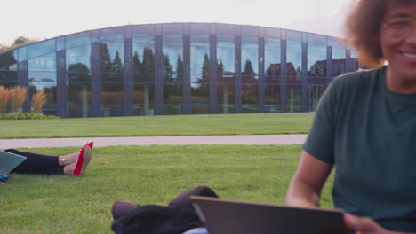 Group-Of-University-Or-College-Students-Sit-On-Grass-Outdoors-On-Campus-Talking-And-Working