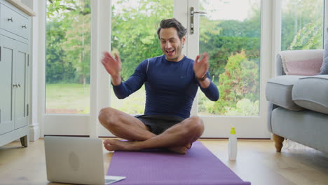 Reifer-Männlicher-Lehrer-Sitzt-Zu-Hause-Auf-Matte-Mit-Laptop-Und-Gibt-Online-Yoga-Kurs
