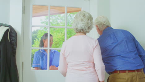 Älteres-Paar-Begrüßt-Eine-Krankenschwester-Oder-Pflegekraft,-Die-In-Uniform-Einen-Hausbesuch-An-Der-Tür-Macht
