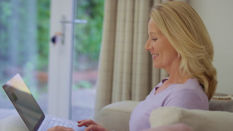 Mature-woman-at-home-sitting-on-sofa-using-laptop-computer---shot-in-slow-motion
