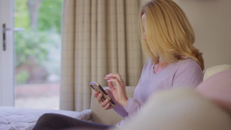 Mature-woman-at-home-sitting-on-sofa-using-mobile-phone---shot-in-slow-motion