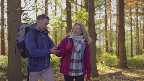Mature-couple-walking-through-fall-or-winter-countryside-looking-at-navigation-app-on-mobile-phone-to-find-way---shot-in-slow-motion
