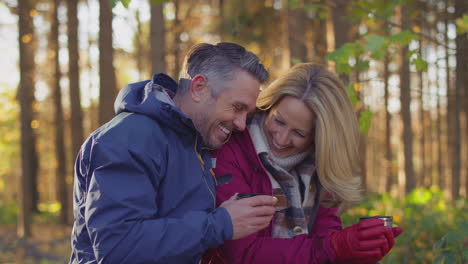 Loving-mature-couple-stop-for-rest-and-hot-drink-on-walk-through-fall-or-winter-countryside---shot-in-slow-motion