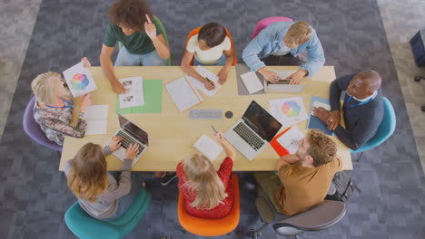 Overhead-Shot-Of-University-Or-College-Students-Sitting-Around-Table-With-Tutors-In-Lesson