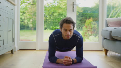 Mature-Man-In-Exercise-Clothing-Lying-On-Mat-In-Lounge-At-Home-Doing-Yoga