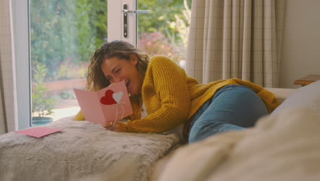 Woman-In-Cosy-Warm-Jumper-Lying-On-Sofa-At-Home-Lying-On-Sofa-Reading-Romantic-Valentines-Day-Card