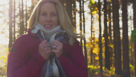 Mature-woman-wrapping-herself-In-warm-coat-on-walk-through-fall-or-winter-countryside---shot-in-slow-motion