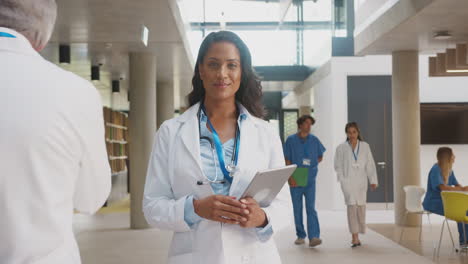 Portrait-Of-Female-Doctor-Wearing-White-Coat-With-Digital-Tablet-In-Busy-Hospital-Building