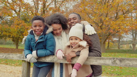 Portrait-of-smiling-family-with-parents-with-children-leaning-on-gate-on-walk-through-autumn-countryside-together---shot-in-slow-motion