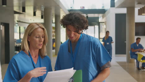 Medical-Staff-In-Scrubs-Discussing-Patient-Notes-Have-Informal-Meeting-In-Busy-Hospital