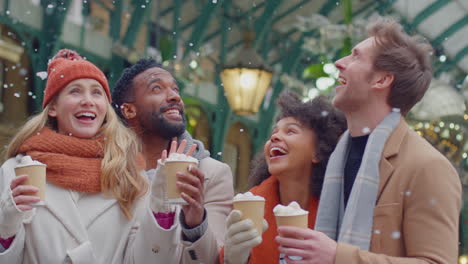 Group-of-friends-drinking-hot-chocolate-with-marshmallows-in-snow-at-outdoor-Christmas-market-in-London's-Covent-Garden---shot-in-slow-motion