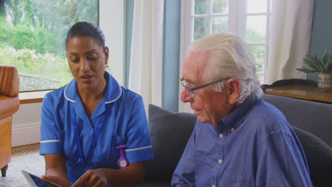 Una-Pareja-De-Ancianos-En-Casa-Con-Un-Hombre-Hablando-Con-Una-Enfermera-O-Una-Trabajadora-De-Atención-Usando-Una-Tableta-Digital