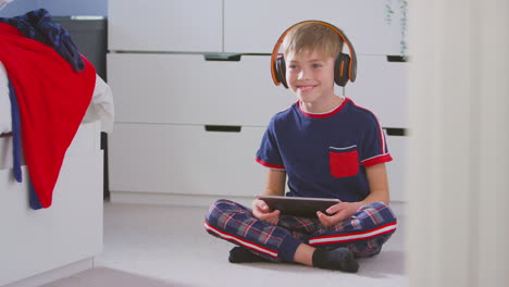 Niño-En-Casa-En-El-Dormitorio-Usando-Auriculares-Inalámbricos-Escuchando-Música-En-Una-Tableta-Digital