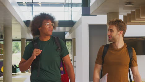 Two-Male-Students-In-Busy-University-Or-College-Building-Talking-As-They-Walk-Along-Corridor