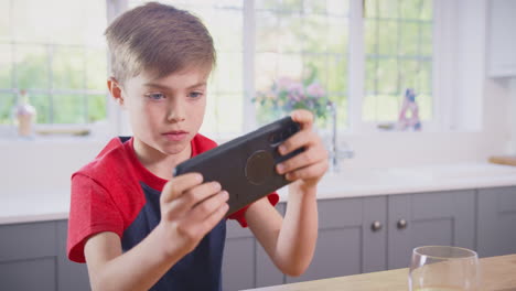 Boy-At-Home-In-Kitchen-Playing-Game-On-Mobile-Phone
