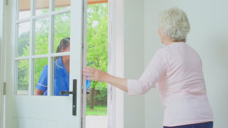 Senior-Woman-At-Home-Using-Walking-Frame-Greeting-Female-Nurse-Or-Care-Worker-In-Uniform-At-Door