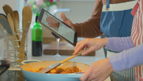 Mature-couple-at-home-following-recipe-on-digital-tablet-in-kitchen-as-they-prepare-meal-together---shot-in-slow-motion