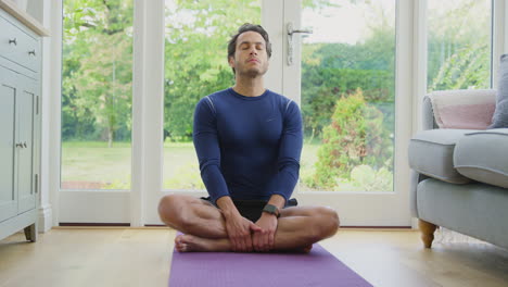 Porträt-Eines-Lächelnden-Reifen-Mannes,-Der-Zu-Hause-In-Yoga-Position-Auf-Einer-Matte-Sitzt-Und-Meditiert