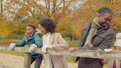 Portrait-of-smiling-family-with-parents-with-children-leaning-on-gate-on-walk-through-autumn-countryside-together---shot-in-slow-motion