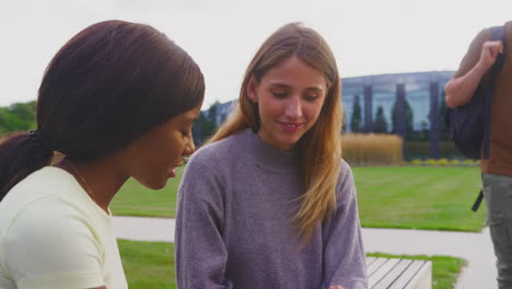 Female-University-Or-College-Students-Sitting-Outdoors-On-Campus-Talking-And-Working-On-Laptop