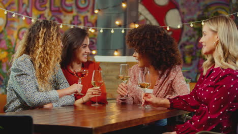 Group-Of-Multi-Cultural-Female-Friends-Sitting-At-Table-Drinking-Wine-Enjoying-Girls-Night-Out