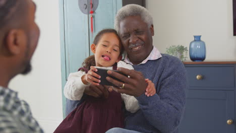 Grandfather-with-grandchildren-playing-game-on-mobile-phone-at-home---shot-in-slow-motion