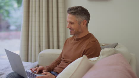 Mature-man-at-home-sitting-on-sofa-using-laptop-computer---shot-in-slow-motion