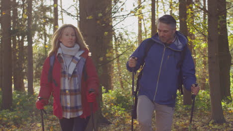 Front-view-of-mature-couple-walking-through-fall-or-winter-countryside-using-hiking-poles---shot-in-slow-motion
