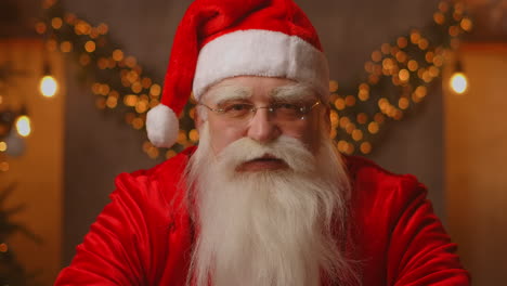 Close-up-of-grey-haired-Santa-Clause-in-glasses-looking-at-camera.-Headshot-portrait-of-funny-old-kind-bearded-Santa-Claus-face.-Saint-Nicholas-greeting-on-Merry-Christmas.-High-quality-4k-footage