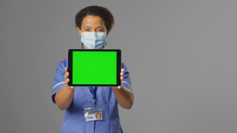 Portrait-Of-Nurse-Wearing-Uniform-And-Face-Mask-Holding-Digital-Tablet-With-Blank-Green-Screen