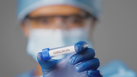 Close-Up-Of-Female-Lab-Research-Worker-Wearing-PPE-Holding-Test-Tube-Labelled-Omicron